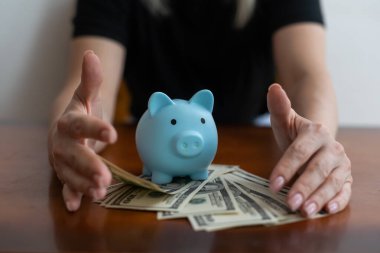 Kadın, para biriktirmek ve finansal konsept için domuzcuğa banknot dolar koyuyor.