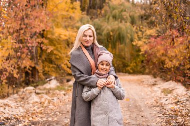 Mutlu aile annesi ve kızı sonbahar yürüyüşünde gülüp oynuyorlar. Anne ve çocuk ilişkileri. Aynı ceketle şık görünümlü bir anne ve kız..