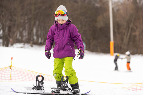 Snowboard Winter Sport. Little kid girl playing with snow wearing warm winter clothes. Winter background.