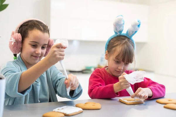 两个女孩用巧克力糖衣装饰饼干 庆祝会期间烹调食物 — 图库照片