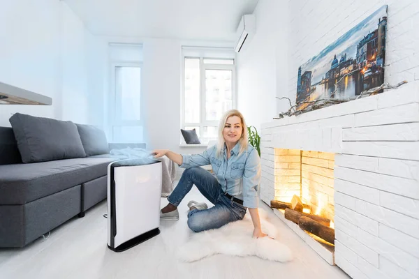 woman turning on and using the modern air purifier in the living room, air purifier is a popular appliance - household electricity. Air purifier can help to purify the air