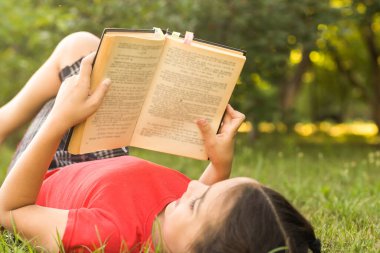 Bahçede kitabı olan küçük bir kız. Çocuk elinde bir kitap okuyor. Yazın açık havada. Kırsal.