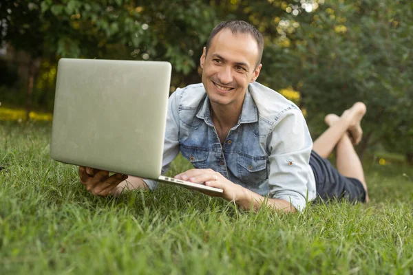高加索人他的恐慌男人使用耳机和坐在草地上与笔记本电脑一起工作 在户外工作的临时工 — 图库照片