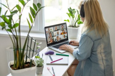 Çekici mutlu genç kız öğrenci ders çalışıyor, masada oturuyor, dizüstü bilgisayar kullanıyor, görüntülü sohbet ediyor, el sallıyor..