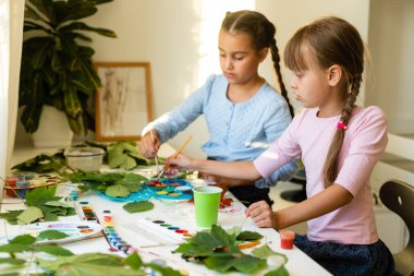 Çocuklar için sonbahar sanatı. Akçaağaç yaprağından yapılmış hayvan tilkisi. Çocuk sanatı ve yaratıcı. Doğal malzemelerden yapılmış el işi. Kızlar boyayla resim yapar.