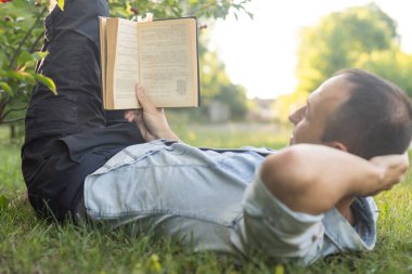 Genç adam çimenlerde uzanıyor, rahatlıyor ve kitap okuyor..