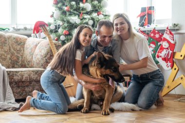 Heyecanlı kız ve ailesi Noel ağacının yanında oturmuş gülümsüyor. Noel zamanı aile.