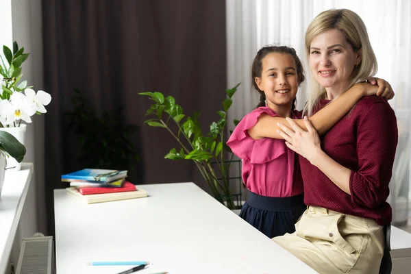 Caring mother calming and hugging little daughter, sitting at desk together, loving mum expressing support, comforting offended preschool girl, children psychologist concept.