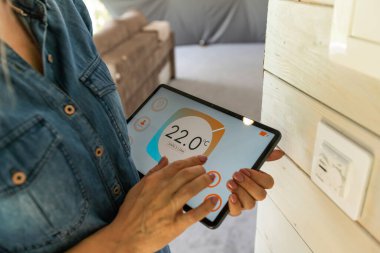 woman holding a tablet computer with system clever house on a screen on the background of the house.