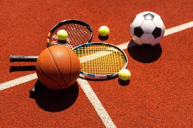 Siyah arkaplanda tenis, basketbol ve futbol ekipmanları ve fotokopi alanı olan bir spor ekipmanı grubu.