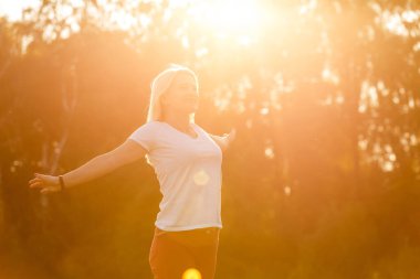 Çekici genç bir kadın, arka planda günbatımıyla parkta eğleniyor.