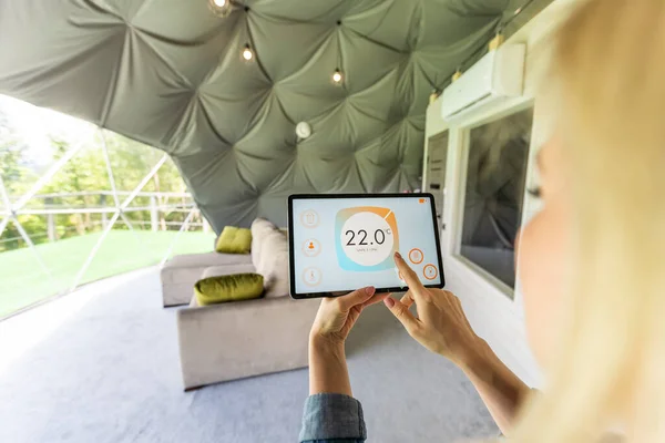 Young woman controlling home light with a digital tablet in the glamping dome tent. Concept of a smart home and light control with mobile devices.