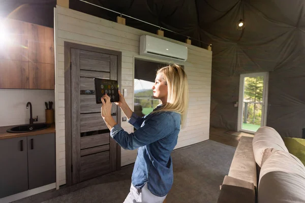Young woman controlling home light with a digital tablet in the glamping dome tent. Concept of a smart home and light control with mobile devices.