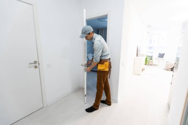 Ön ahşap giriş kapısına bir kilit takıldı. Kapı tokmağı monte eden mavi üniformalı genç çilingir işçisinin portresi. Profesyonel tamir servisi. Bakım Kavramı.