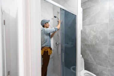 Üniformalı tamirciler banyodaki modern duş kabinini ölçüyorlar.