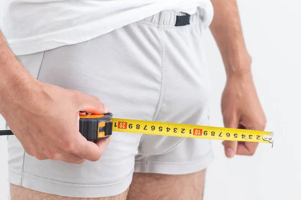 Young man holding tape measure, measuring his penis - focused at the middle of tape measure