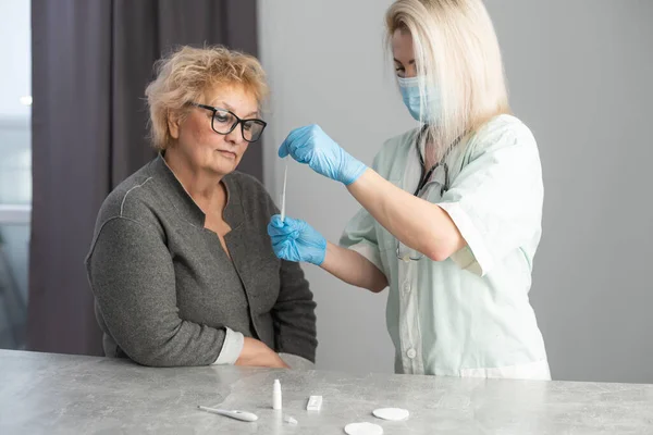 Professional medical worker wearing personal protective equipment testing senior woman for dangerous disease using test stick