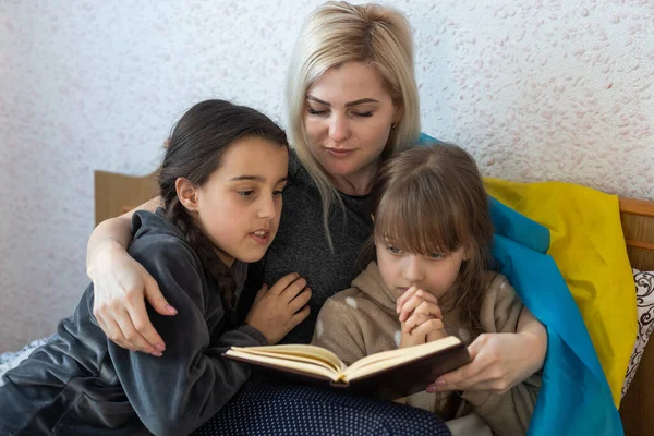 mother and daughter reading a book with the flag of ukraine in bed.