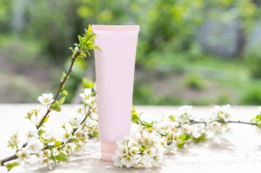 Boş beyaz kozmetik tüpü ve pastel arka planda beyaz çiçekli bahar çiçekli ağaç dalı. Ön görünüm.
