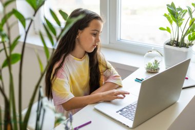 Evde giydiği dizüstü bilgisayarla oturma odasında oturan heyecanlı genç kız. Çevrimiçi Okul Sınavları Konsepti.