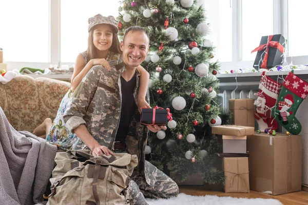 Soldier in uniform decorating Christmas tree with his daughter. An off duty military man spending Christmas holiday with his family at home.