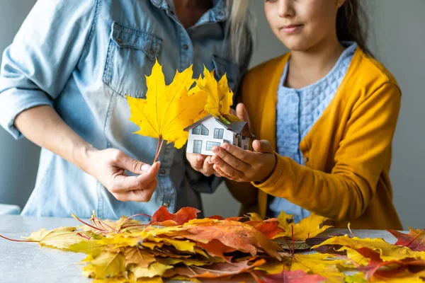 Autumnal Background. Toy house and dried orange fall maple leaves. Thanksgiving banner copy space. Hygge mood cold weather concept. Hello Autumn with family.