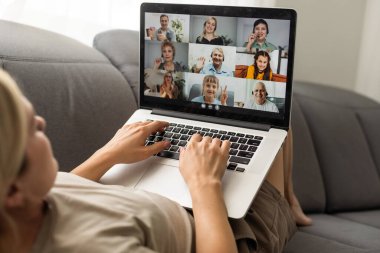 Young woman enjoying video conversation via laptop with eldery mother while sitting on sofa during self isolation for coronavirus prevention