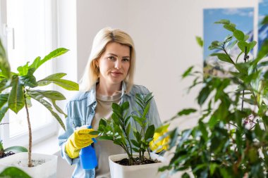 Genç, gülümseyen kadın bahçıvan saksılarla ilgileniyor. Evde bahçe işleri, ev bitkilerini sevmek, serbest çalışmak.