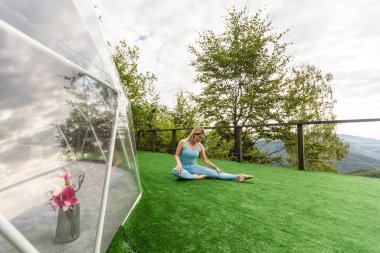 a woman is doing exercises on the terrace of a transparent bubble dome.