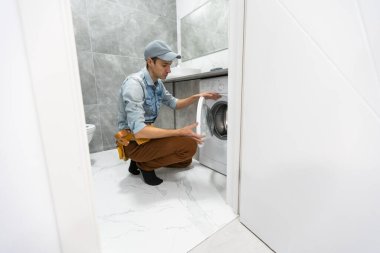 Profesyonel alet çantalı genç ve yakışıklı tamirci banyodaki çamaşır makinesini tamir ediyor.
