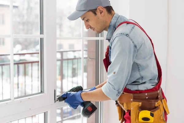 Yakışıklı genç adam yeni bir inşaat alanına pencere takıyor.