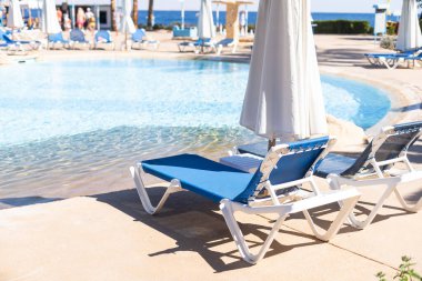 Temiz suyu olan bir yüzme havuzu, hiç kimse. Kare şeklinde bir havuz, mavi fayanslar, çekmeceler ve güvertelerde güneşlik, insan yok. Su yüzeyi. Genel bakış. Yaz arkaplanı