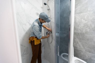 Üniformalı tamirciler banyodaki modern duş kabinini ölçüyorlar.