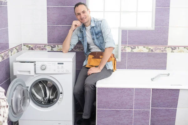 working man plumber repairs a washing machine in laundry.