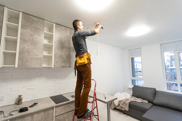 electrician, a male electrician is standing on the stairs holding wiring in his hands and stripping, repairing light at home, repair work, call master, electrician man repairing light.