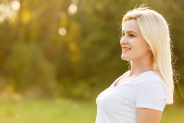 Çekici genç bir kadın, arka planda günbatımıyla parkta eğleniyor.