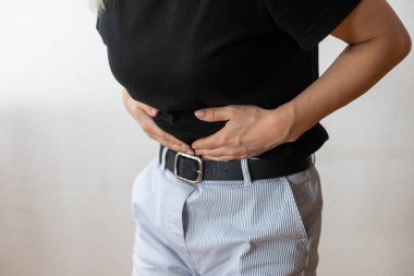 A woman standing in front of a white background and holding her hands on her belly