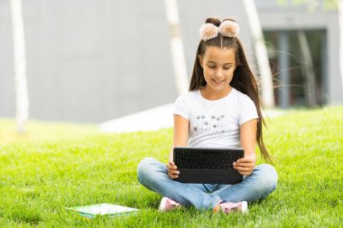 çimenlerin üzerinde oturan ve tablet pc oynarken küçük kız.