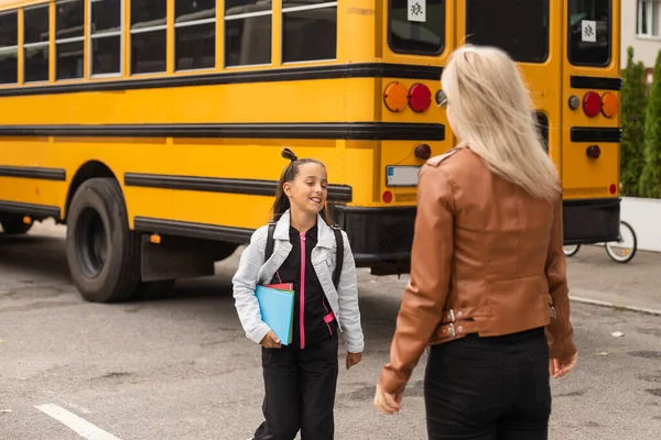 Parent and pupil of primary school. Woman and girl with backpack behind the back. Beginning of lessons. First day of fall