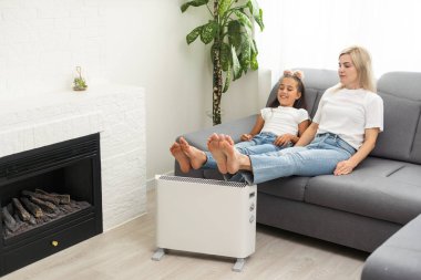 Electric heater at home. Young family warms his frozen hands near a heating radiator.