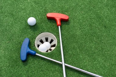 Mini-golf clubs and balls of different colors laid on artificial grass.