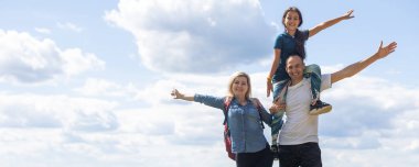 Family standing with arms around on top of mountain, looking at beautiful summer mountain landscape. People enjoying view