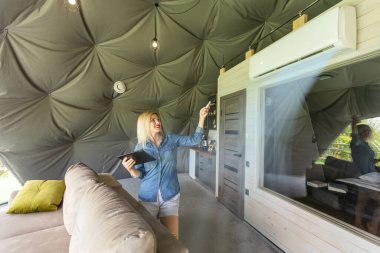 Young woman using smartphone home application on tablet computer when setting temperature in her apartment.