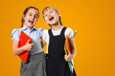 Education Concept. Set portrait of diverse schoolchildren holding stack of academic books and wearing backpack, yellow orange color studio background.