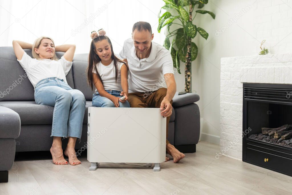 Electric heater at home. Young family warms near a heating radiator