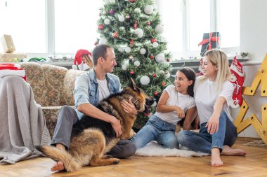 Mutlu Noeller ve mutlu yıllar. Köpekli mutlu aile evde güzel bir Noel ağacının yanında oturmuş yeni yılı bekliyor.