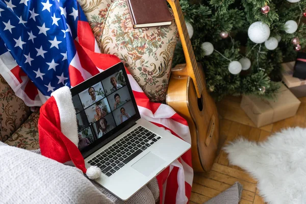 Online party with loved ones from USA. Celebrating Christmas video chat. Virtual party via video messenger. Americans new year are video chatting. New Year gifts and flag of America next to computer.