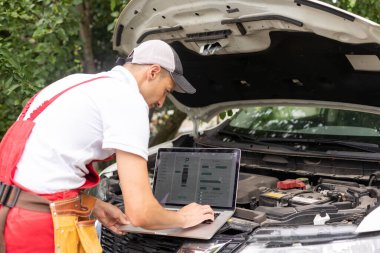 Tamirci, dizüstü bilgisayarı kullanarak kapatıyor. Akort onarımı, araba motoru otomobil parçalarını tamir ediyor. Atölye garajı destek servisindeki aletleri genel iş üniformasında kullanıyor..