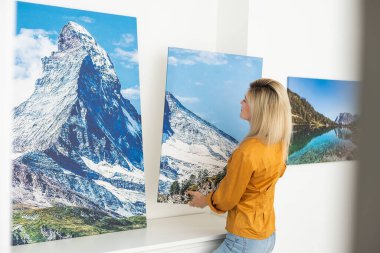 Galeri ambalajlı tuval baskısı. Kadın fotoğrafçılığı beyaz duvara asıyor. Ellerinde resim bezi izi var..