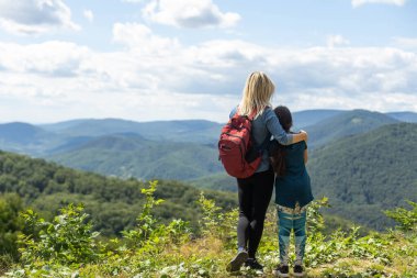 Mother and child with a backpack enjoying in the mountains.The concept of family travel, adventure, and tourism. Lifestyle and hiking autumn vacations outdoor. Back view